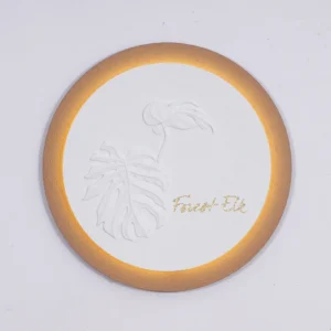 Monstera Circular LED wall decor featuring 3D embossed monstera and anthurium leaves in white plaster, warm gold backlit rim, framed botanical wall decor