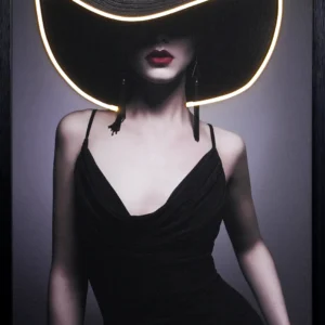 Black Hat Mystique LED wall decor featuring a fashion portrait of a woman in a wide brim black hat with warm gold LED outline, deep red lips, tasseled drop earrings and black slip dress on grey background, framed wall decor